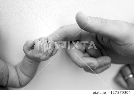 The newborn baby has a firm grip on the parent's finger after birth. Close-up little hand of child and palm of mother and father. Parenting, childcare and healthcare concept. Black and white photo. The newborn baby has a firm grip on the parent's finger after birth. Close-up little hand of child and palm of mother and father. Parenting, childcare and healthcare concept. Black and white photo. 117879304