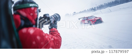 Focused man in red jacket, with professional camera capturing dynamic photo of race car speeding through the snow road. 117879597