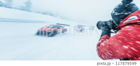Focused man in red jacket, with professional camera capturing dynamic photo of racing car in motion on snowy road 117879599