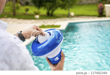 Pool float and chlorine tablets for pool maintenance. Hands holding a pool chlorine dispenser. Hand of a pool disinfection worker holding a dispenser with a chlorine tablet. Hands holding a dispenser Pool float and chlorine tablets for pool maintenance. Hands holding a pool chlorine dispenser. Hand of a pool disinfection worker holding a dispenser with a chlorine tablet. Hands holding a dispenser 117882260