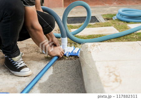 Pool suction hose installation. Person connecting pool hose handle. Man connecting the handle on the pool vacuum. Suction equipment connection for swimming pool 117882311