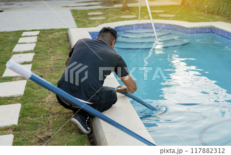 Maintenance person cleaning swimming pool with suction hose. Cleaning and maintenance of swimming pools with suction hose. Crouched man cleaning swimming pool with vacuum hose Maintenance person cleaning swimming pool with suction hose. Cleaning and maintenance of swimming pools with suction hose. Crouched man cleaning swimming pool with vacuum hose 117882312