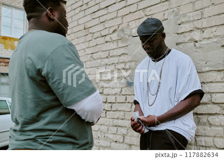 Man leaning on old garage wall while counting money, customer waiting for him calmly Man leaning on old garage wall while counting money, customer waiting for him calmly 117882634