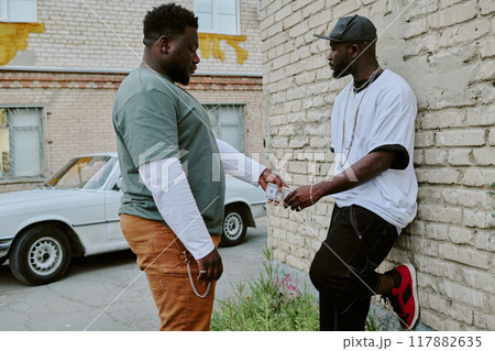 African American man giving wad of cash to guy who leaning on old garage African American man giving wad of cash to guy who leaning on old garage 117882635