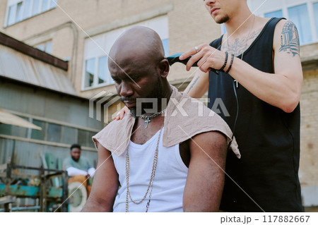 Low angle shot of unrecognizable tattooed male hands shaving head of serious man 117882667