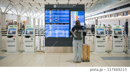 Young Asian woman in international airport looking at flight information board, checking her flight 117889215