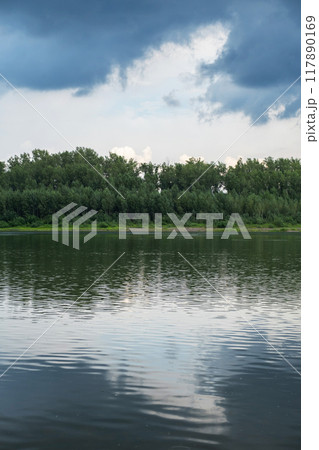 Serene landscape of forest and calm lake, with reflections of trees on the water. 117890169