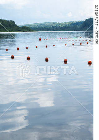 Orange buoys floating on a calm lake with forested shore in the background. Orange buoys floating on a calm lake with forested shore in the background. 117890170