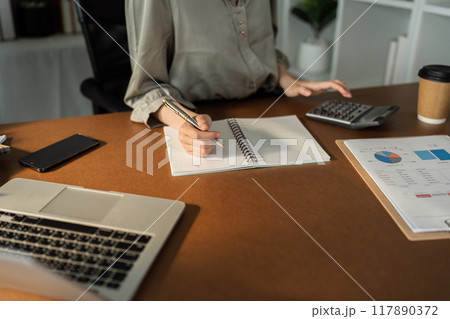 Asian business woman Calculate report with calculator. Take note. Have notepad to remember to do financial report or profit. 117890372