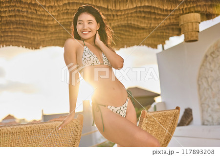 Smiling Woman in Floral Bikini Enjoying Sunny Beach Vacation Under Straw Umbrella Smiling Woman in Floral Bikini Enjoying Sunny Beach Vacation Under Straw Umbrella 117893208