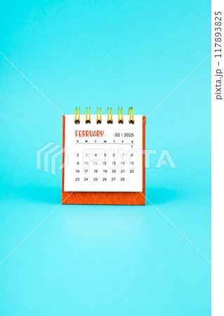 February 2025 white desk calendar on blue background. 117893825