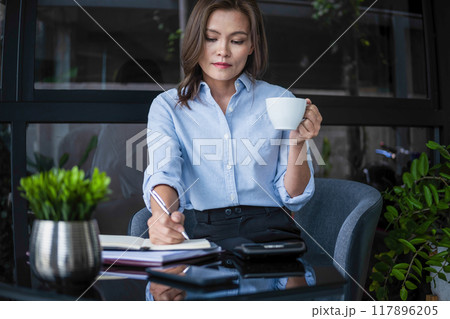 Businesswoman working while enjoying coffee. 117896205