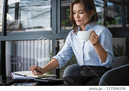 Businesswoman working while enjoying coffee. 117896206