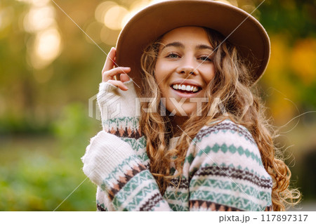 Happy woman in stylish sweater and hat outdoors in autumn park on plaid. Woman enjoys autumn nature. 117897317