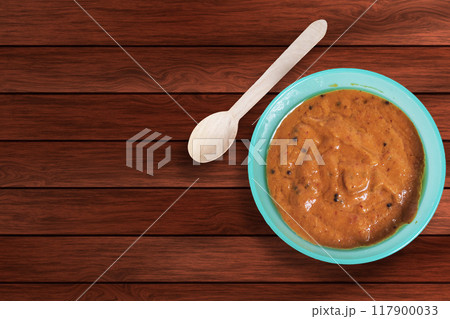 Onion chutney in a blue bowl with wooden spoon on a table. Top view. 117900033