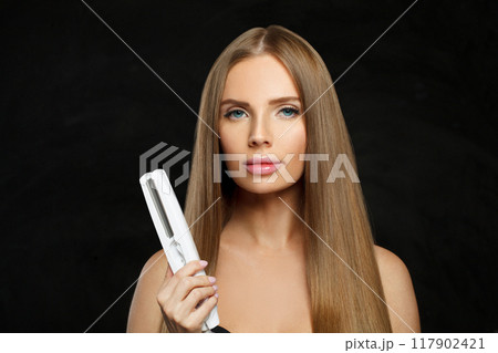 Stylish smiling woman with long straight healthy hairstyle using straightening iron Stylish smiling woman with long straight healthy hairstyle using straightening iron 117902421