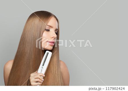 Lovely brunette lady with straight hair holding straightening iron on white background. 117902424