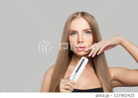 Nice fashion model woman using hair straighteners iron on white background. 117902425