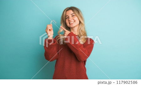 Happy young woman showing invisible braces in blue studio 117902586