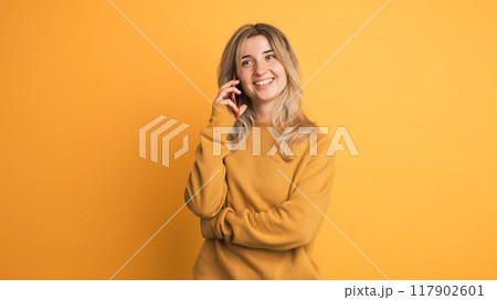 Cheerful woman with blonde hair smiling and speaking on telephone on yellow background 117902601
