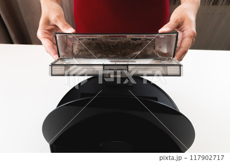 Maintenance of a smart robot vacuum cleaner. Women's hands maintain and clean a round robot vacuum cleaner. Organization of uninterrupted operation of a home cleaner 117902717