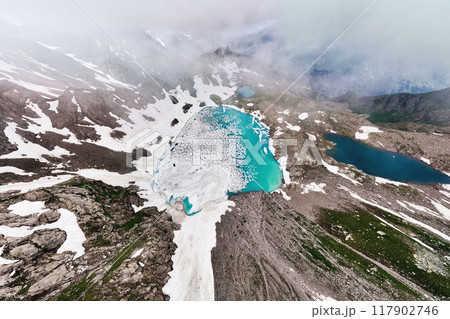 Wide-angle aerial view of high mountain lakes surrounded by snow-covered rocks. Crazy view of two turquoise mountain lakes. Sources of clean water high in the mountains Wide-angle aerial view of high mountain lakes surrounded by snow-covered rocks. Crazy view of two turquoise mountain lakes. Sources of clean water high in the mountains 117902746