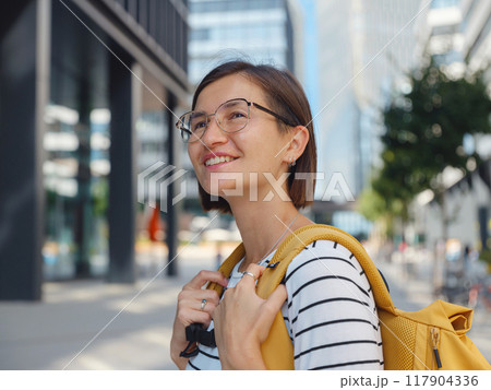 Asian woman with yellow backpack over background of modern urban architecture in Vienna. charming pensive female hipster admire cityscape of modern Vienna city 117904336