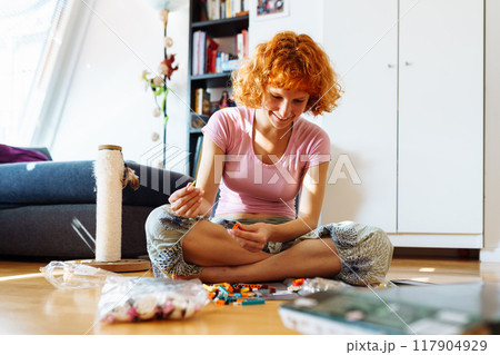 teenage girl assembles construction set according to instructions sitting on floor in room teenage girl assembles construction set according to instructions sitting on floor in room 117904929