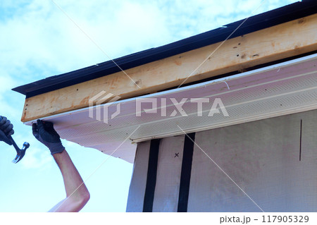Worker installs plastic vinyl soffit on roof corner of rafters house Worker installs plastic vinyl soffit on roof corner of rafters house 117905329