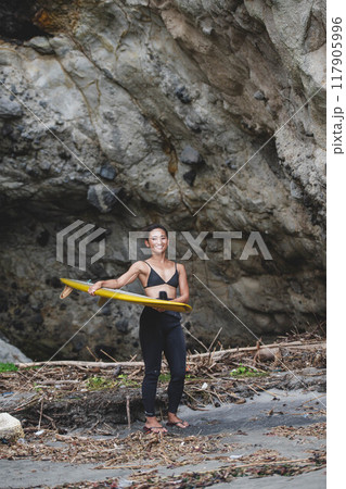 岩場でサーフボードを持っている若い女性 117905996