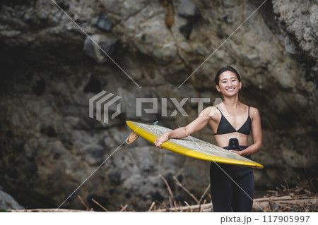 岩場でサーフボードを持っている若い女性 117905997