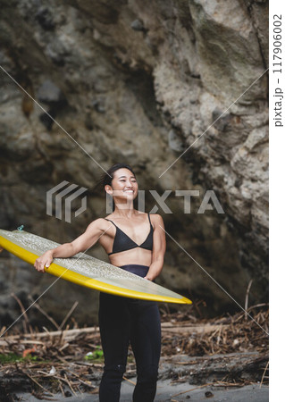 岩場でサーフボードを持っている若い女性 117906002