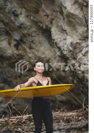 岩場でサーフボードを持っている若い女性 岩場でサーフボードを持っている若い女性 117906003