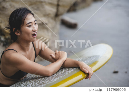岩場でサーフボードを持っている若い女性 117906006