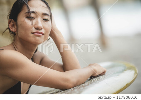 岩場でサーフボードを持っている若い女性 117906010