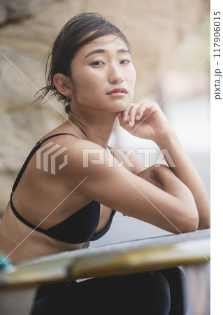 岩場でサーフボードを持っている若い女性 117906015