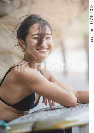 岩場でサーフボードを持っている若い女性 117906018