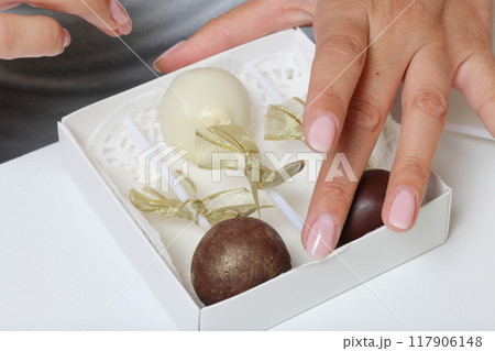 Woman puts cake pops in a gift box. Scissor wand candy. Candies are decorated with ribbons. 117906148