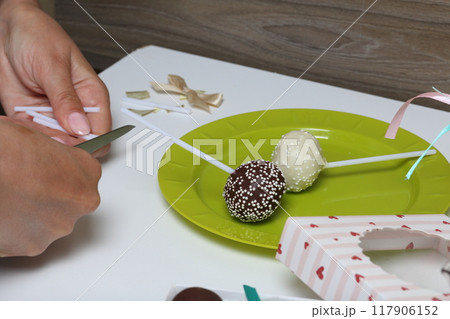 Woman puts cake pops in a gift box. Scissor wand candy. Woman puts cake pops in a gift box. Scissor wand candy. 117906152