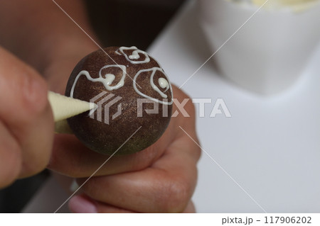 A woman decorates with the help of white chocolate popcake glazed with dark chocolate. 117906202