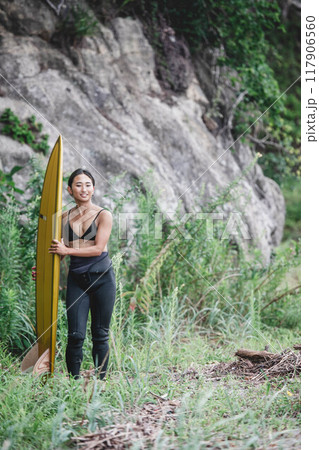 サーフボードを持って自然の中にいる若い女性 117906560