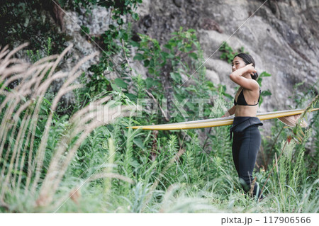 サーフボードを持って自然の中にいる若い女性 117906566