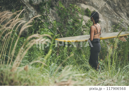 サーフボードを持って自然の中にいる若い女性 117906568