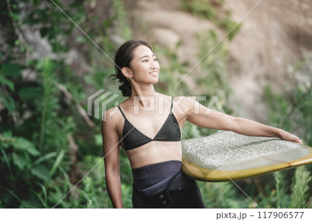 サーフボードを持って自然の中にいる若い女性 117906577