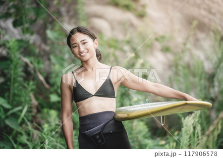 サーフボードを持って自然の中にいる若い女性 117906578