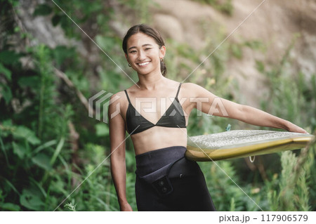 サーフボードを持って自然の中にいる若い女性 117906579