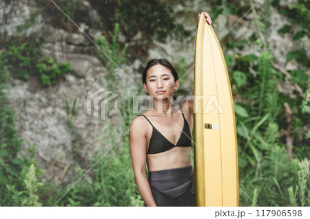 サーフボードを持って自然の中にいる若い女性 117906598