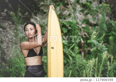 サーフボードを持って自然の中にいる若い女性 117906599
