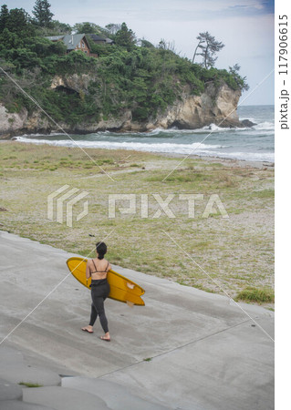 サーフボードを持って海辺を歩く若い女性 117906615