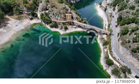 A serene aerial view of a picturesque bridge over turquoise waters near a charming abandoned building surrounded by rocky landscape 117908056